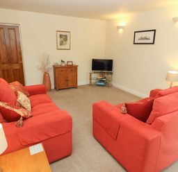 A living room with two red sofas a wooden cabinet a television on a glass stand and wall lights at Kirkstones in Keswick
