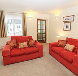 A living room with two red sofas and cushions a wooden side table a window with curtains and a glass door at Kirkstones in Keswick