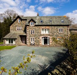 A large stone house with multiple windows and a gravel driveway surrounded by trees at Tethera in Keswick