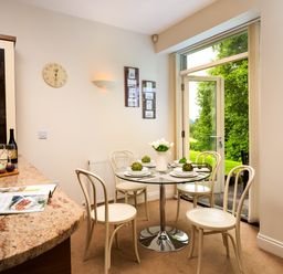 A dining area with a round glass table set for four next to an open door showing greenery outside at Tethera in Keswick