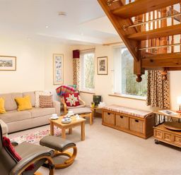 A living room with a beige sofa and yellow cushions a wooden coffee table and armchair under wooden stairs at Lingmoor View in Chapel Stile