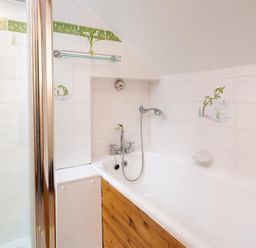 A bathroom with a white bathtub wood paneling shower area and white tiled walls with green border at Lingmoor View in Chapel Stile