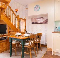 A dining area with a wooden table set for four near a wooden staircase and a kitchen counter at Lingmoor View in Chapel Stile