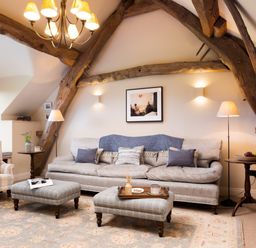 A living room with a sofa chair two ottomans and wooden beams at High Cunsey Farm in Far Sawrey