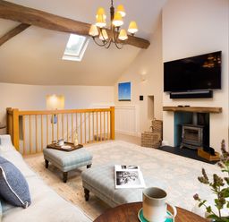 A living room with a sofa, ottomans, a wood stove, and a mounted TV at High Cunsey Farm in Far Sawrey