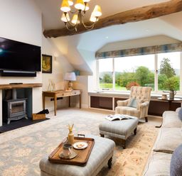 A living room with a sofa armchair ottomans a fireplace and a large window at High Cunsey Farm in Far Sawrey