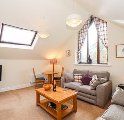 A living room with a sofa, coffee table, TV, small dining table with chairs, floor lamp, and triangular window with curtains at Squirrel Bank in Ambleside