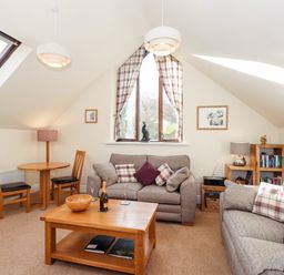 A living room with two sofas, a wooden coffee table, dining table with two chairs, bookshelf, and a window with curtains at Squirrel Bank in Ambleside