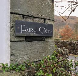 A stone wall with a sign reading Fairy Glen near a driveway and trees at Fairy Glen in Grasmere near Ambleside