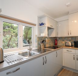 A kitchen with a sink under a window a kettle a toaster a microwave and cabinets at Larch Cottage in Hawkshead