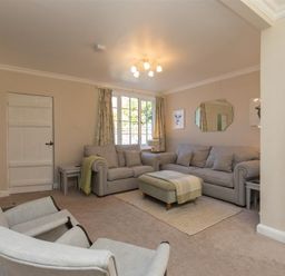 A living room with two sofas a cushioned ottoman two armchairs a wall-mounted tv and a window at Crozier Cottage in Grasmere