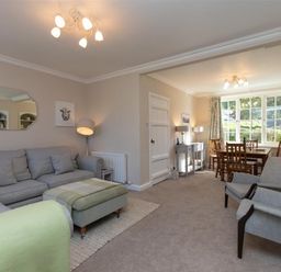 A living room with gray sofa and green ottoman adjacent to a dining area with wooden table and chairs at Crozier Cottage in Grasmere