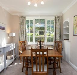 A dining room with a wooden table and chairs next to a window with floral curtains at Crozier Cottage in Grasmere