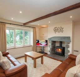 A living room with two leather sofas a wooden coffee table stone fireplace and a window at Dancing Beck Cottage in Millbeck