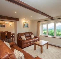 A living room with two leather sofas a wooden coffee table and a window showing a mountain view at Dancing Beck Cottage in Millbeck