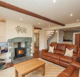 A living room with a wood burning stove and two brown leather sofas at Dancing Beck Cottage in Millbeck