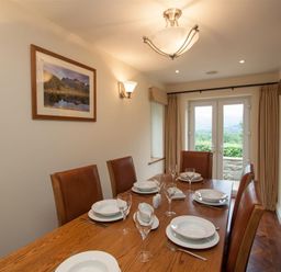 A dining room with a wooden table set with plates and glasses and leather chairs near a glass door at Dancing Beck Cottage in Millbeck