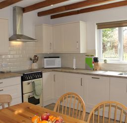 A kitchen with wooden chairs a fruit bowl on a wooden table a stove microwave and a window at Bandol in Braithwaite