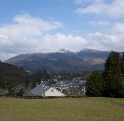 A landscape with a grassy field in the foreground houses and trees in the middle and mountains with snow patches in the background at Bandol in Braithwaite