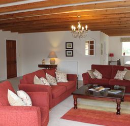 A living room with red sofas and armchairs around a wooden coffee table under wooden ceiling beams at Bandol in Braithwaite