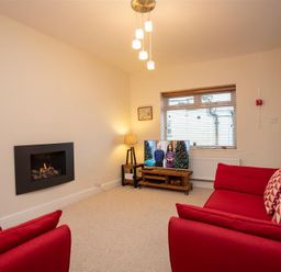 A living room with two red sofas a wall-mounted fireplace a wooden TV stand with a television and a window at Gable End in Braithwaite