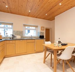 A kitchen with wooden cabinets a dining table with four chairs and kitchen appliances at Gable End in Braithwaite