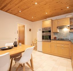 A kitchen with wooden cabinets a wooden dining table and white chairs at Gable End in Braithwaite