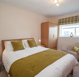 A bedroom with a double bed green cushions and throw two bedside tables wooden wardrobe wicker chair and window at Gable End in Braithwaite