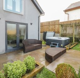 Outdoor patio with wicker furniture and a hot tub by a fenced garden at Meadow View in Tyn-y-Gongl near Benllech