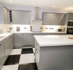 A kitchen with grey cabinets a white countertop and black and white checkered floor at Meadow View in Tyn-y-Gongl near Benllech