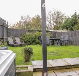 A garden with lawn chairs a table and chairs a hot tub and wooden fencing at Meadow View in Tyn-y-Gongl near Benllech