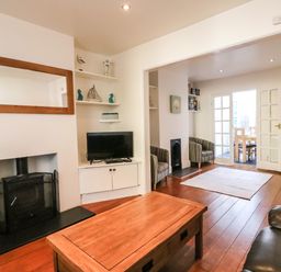 A living room with a wood stove coffee table television and armchairs leading to a dining area at South Harbour Cottage in Weymouth