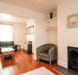 A living room with sofas a wooden coffee table a striped armchair and a fireplace at South Harbour Cottage in Weymouth