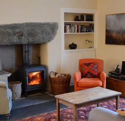 A living room with a wood burning stove an orange armchair a wooden coffee table and a striped armchair at Thomas Cottage in Hartsop