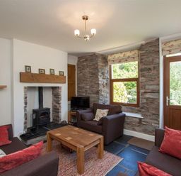 A living room with brown sofas a wooden coffee table a small fireplace and stone wall at Robins Nest in Coniston