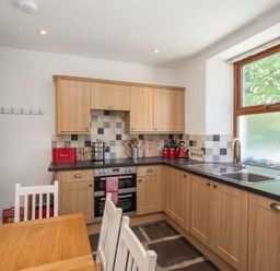 A kitchen with wooden cabinets black countertops a stainless steel sink and window and a wooden dining table with white chairs at Robins Nest in Coniston