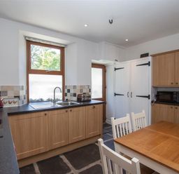 A kitchen with wooden cabinets a wooden table and white chairs a window above the sink a microwave and toaster on countertops at Robins Nest in Coniston