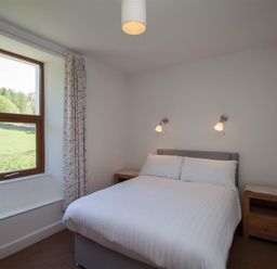 A bedroom with a double bed two bedside tables and a window with curtains at Robins Nest in Coniston