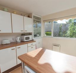 A kitchen with white cabinets a microwave kettle toaster and a window showing outdoor plants at Brimbles in Keswick