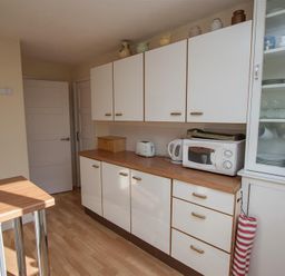 A kitchen with white cabinets a wooden countertop a microwave kettle toaster and a glass cupboard with dishes and cups at Brimbles Keswick