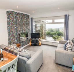 A living room with grey sofas a wooden table a tv and large window at Helm Crag in Grasmere
