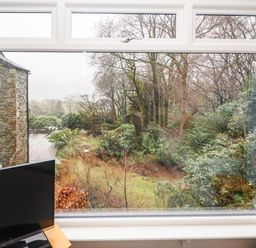 A window view showing a stone building patio and garden area with trees and bushes at Helm Crag in Grasmere