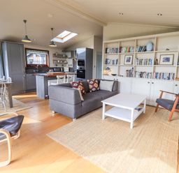 An open plan living area with a grey sofa a white coffee table a dining table and chairs a kitchen with grey cabinets and a wall of bookshelves at How Beck in Hawkshead