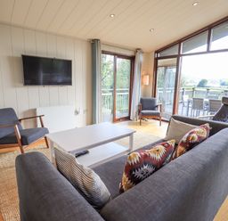 A living room with a gray sofa a white coffee table two armchairs a wall-mounted TV and large windows at How Beck in Hawkshead