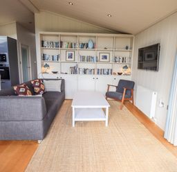 A living room with a gray sofa, armchair, white coffee table, bookshelf, and wall-mounted television at How Beck in Hawkshead