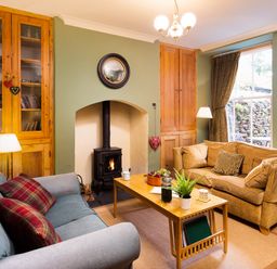 A living room with two sofas wood burning stove coffee table and built in cupboards at Greystones in Bowness