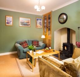 A living room with two sofas a wooden coffee table a wood burning stove and framed pictures on the walls at Greystones in Bowness