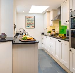 A kitchen with white cabinets black countertops a cutting board with vegetables a built in oven and a green backsplash at Greystones in Bowness