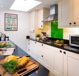 A kitchen with white cabinets black countertops a microwave stove a sink with vegetables and bread on the counter and a manifesto poster on the wall at Greystones in Bowness