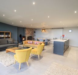 An open plan living room and kitchen with a gray sofa yellow chairs a glass coffee table a dining table and kitchen island at Gillside in Millbeck